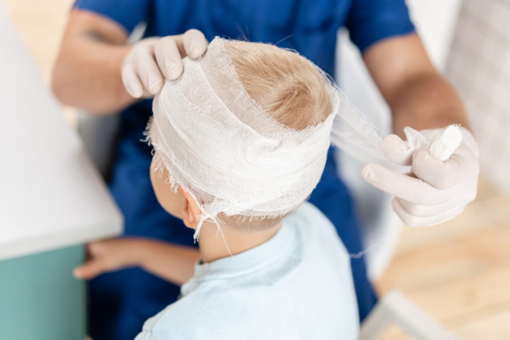 boy getting his head assessed and wrapped by a doctor