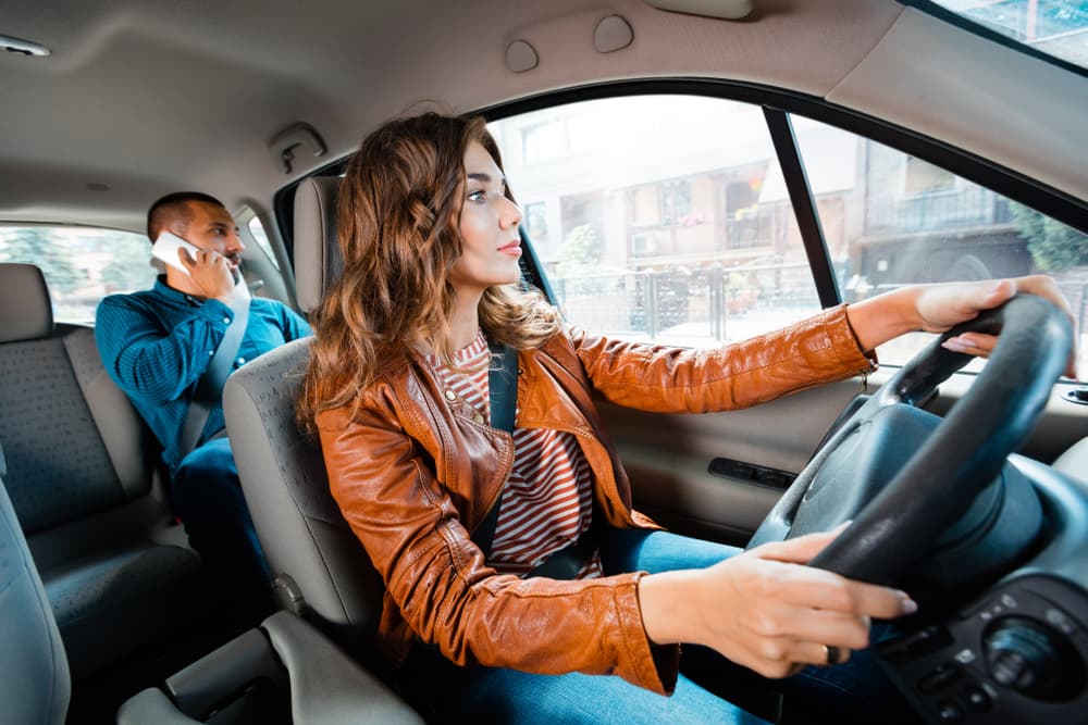 In the background, a male passenger chats on his mobile phone while a female taxi driver navigates through the city streets.